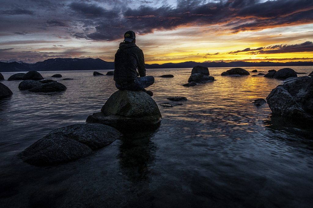 Person Sitting on Rock on Body of Water