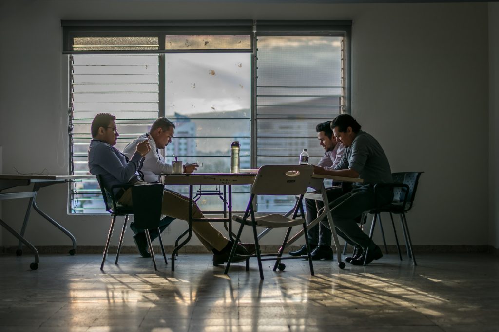 Four Men Sitting in Front of Table Near Glass Window