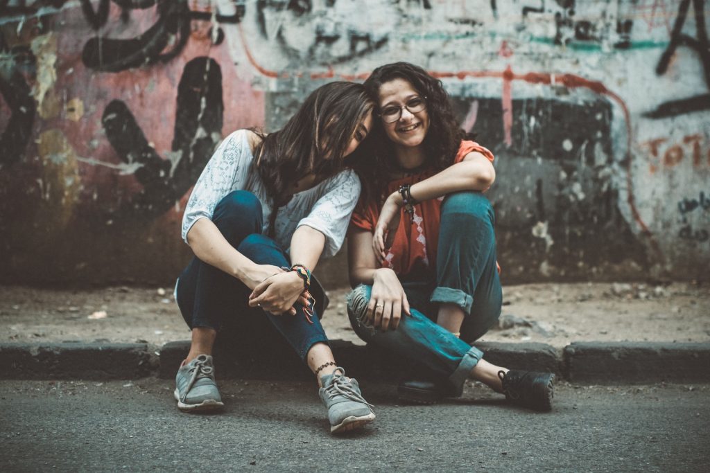 Two Women Sitting on Pavement Near Painted Wall