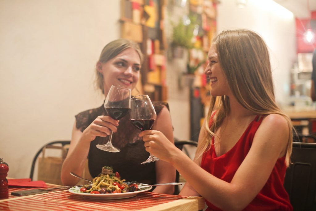 Two Women Holding Long-stem Wine Glasses With Red Liquid