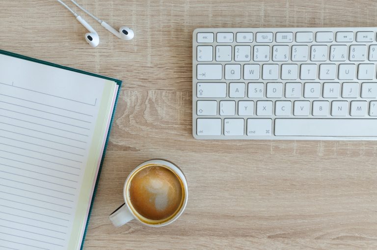 coffee latte near white wireless keyboard and Apple EarPods on the table photography