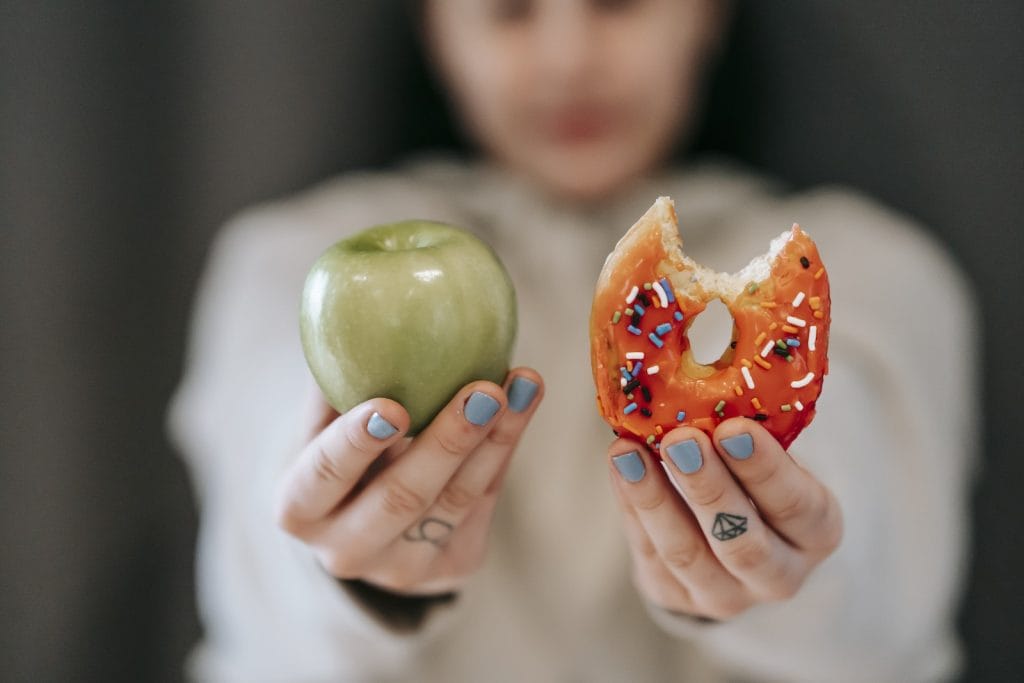 Woman showing apple and bitten doughnut