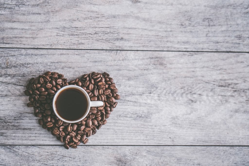 coffee filled white ceramic mug beside brown coffee beans on beige wooden surface