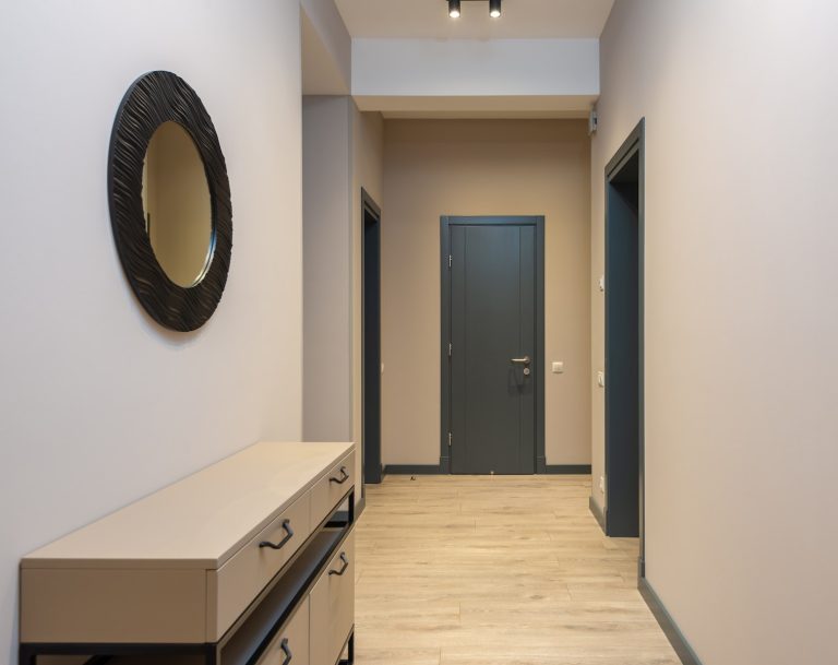 Round mirror hanging above wooden cabinet in spacious corridor of contemporary apartment with parquet floor and beige walls